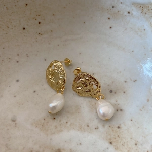 Close-up of baroque pearl earrings with irregular hammered gold metal on a ceramic tray