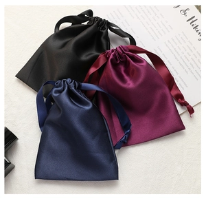 Three satin drawstring pouches in black, burgundy, and dark blue on a textured surface
