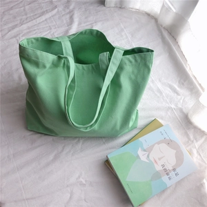 Vue de dessus d'un grand sac cabas en toile vert clair posé sur un tissu blanc doux