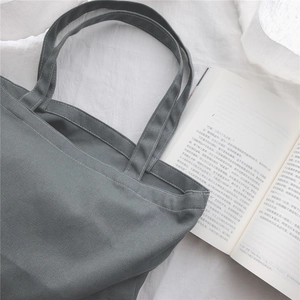 Détail d'un sac cabas en toile gris foncé sur un fond en lin blanc de style minimaliste