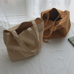 Détail de grands sacs cabas en toile beige et caramel sur un fond textile doux et naturel