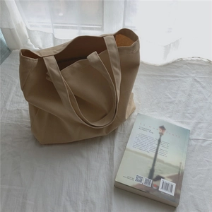 Détail d'un sac cabas minimaliste en toile beige montrant la texture coton et les poignées