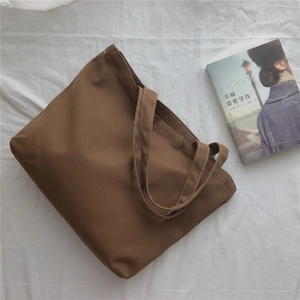 Vue à plat d'un sac cabas en toile marron sur des draps blancs avec un livre décor