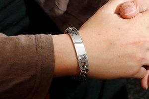 Close-up of a silver men's stainless steel curb chain bracelet with a curved metal ID plate