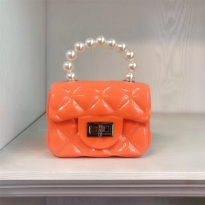 Close-up of an orange mini jelly bag with quilted texture and a white pearl handle