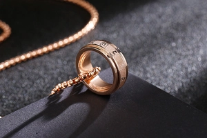 Close-up of rose gold spinning ring with mantra engraving on a matte black background