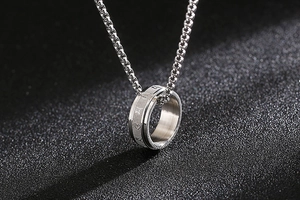 Detail of silver box chain with rotating stainless steel Sanskrit ring pendant on dark background
