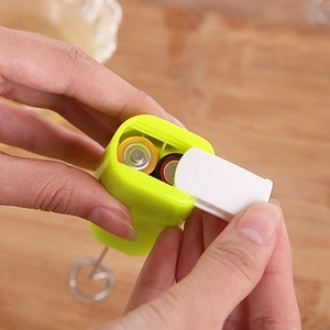 Lime green handheld electric milk frother showing AA battery compartment on wood desk