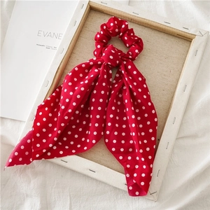 Detail of red polka dot hair scrunchie with long ribbon on a rustic wooden frame