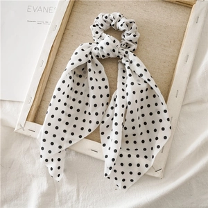 Detail of white and black polka dot silk scrunchie with long ribbons on wooden frame