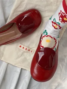Detail of burgundy flat shoes with round buckle worn with floral Tabi split-toe socks