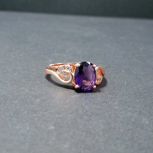 Detail shot of an oval purple gemstone ring with leaf patterns on a rose gold band