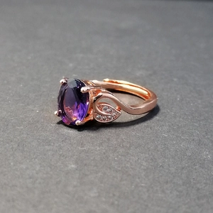 Macro view of rose gold ring with oval purple gemstone and leaf-shaped diamond accents