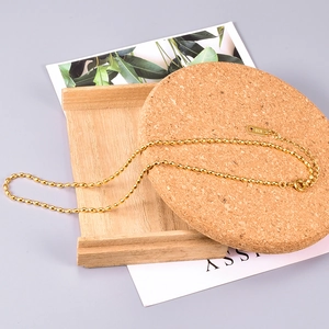 Close-up of minimalist 18K gold bead chain necklace with lobster clasp on wood background