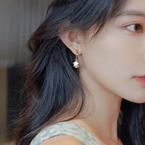 Star charm earrings in gold and white on a model's ear with a minimalist look