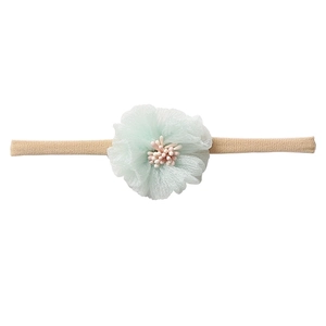 Close-up of a soft beige nylon baby headband with a light green chiffon flower decoration