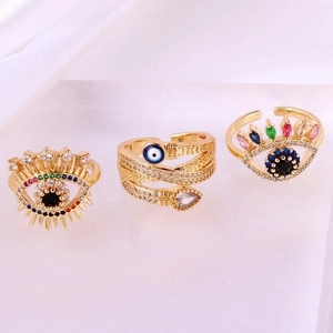 Three gold evil eye rings with colorful cubic zirconia and eyelash details on white silk