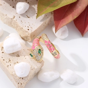 Detailed view of snake ring with pink enamel, green gemstone eyes and gold plating
