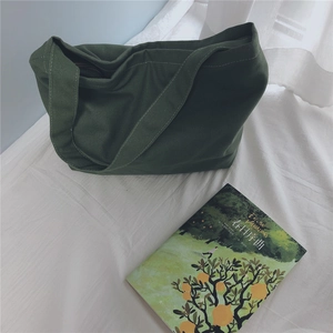 Detailed view of a dark green canvas tote bag on a white bed with books