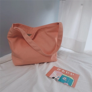 Detail of minimalist peach pink canvas tote bag with wide strap on soft white bedding