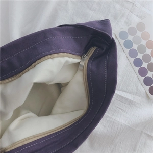Detailed close-up of dark purple canvas tote bag featuring silver metal zipper and white lining