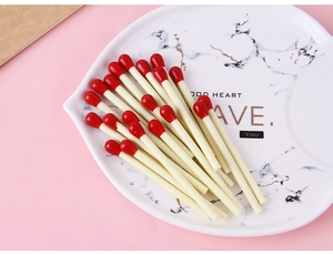 Creative matchstick ballpoint pens with red tips on a marble tray over a pink background