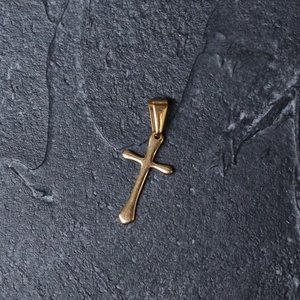 Close-up of a minimalist gold-plated stainless steel cross pendant on a textured dark background