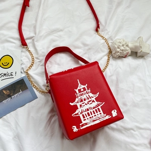 Detail of red crossbody bag with white pagoda print and gold chain strap on white fabric