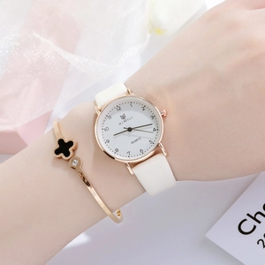 Detail shot of a minimalist gold watch with white leather strap and clover bracelet set