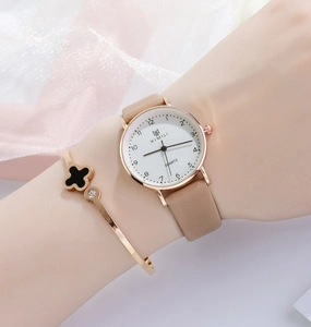 Close-up of minimalist rose gold watch with tan leather strap and clover bracelet