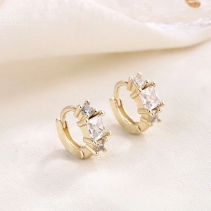 Golden earrings set with square clear zircon and round crystals on textured fabric