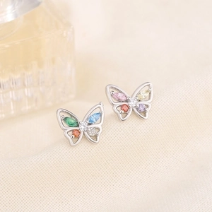 Close-up of butterfly stud earrings with colorful zircons on a beige textured fabric