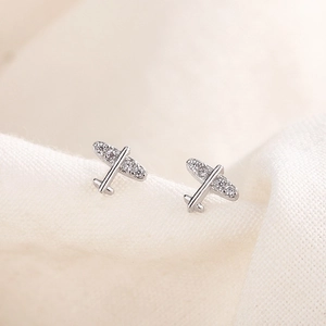Cute mini silver airplane stud earrings with white crystal wings on fabric background