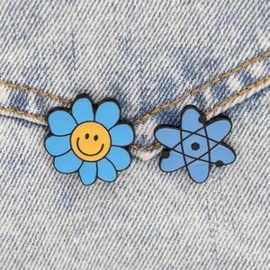 Detail of blue sunflower smiley and atomic enamel pins on light denim jacket fabric