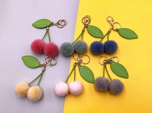 Flat lay of 6 colors of plush cherry keychains with green leaves and gold hardware
