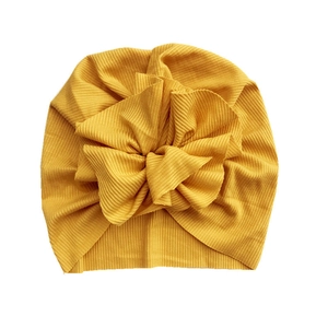 Detail of baby turban hat showing ribbed ginger yellow fabric and large knit flower decor
