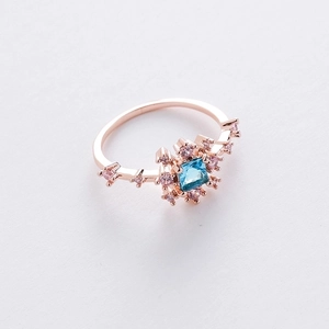 Detail of rose gold ring with blue square gemstone and pink zircon floral accents