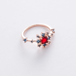 Macro shot of rose gold flower ring featuring a square red stone and blue crystal accents