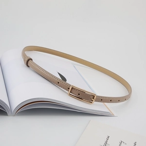 Detail of slim beige leather belt with golden square buckle on aesthetic magazine background