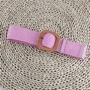 Detail of pink woven elastic waist belt with square straw buckle on a textured mat