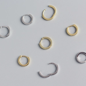 Detalle de pendientes de aro minimalistas en plata S925 dorada y plateada sobre fondo gris