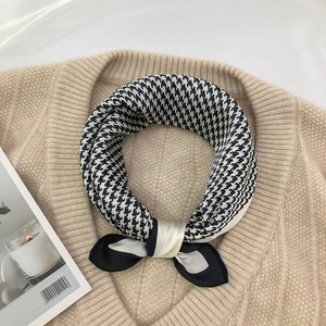 Detail of black and white houndstooth silk scarf tied in a bow on a beige sweater