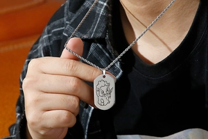 Close-up of a stainless steel dog tag necklace featuring a cartoon sheep engraving