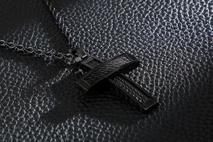 Detail of black stainless steel cross pendant with twisted metal inlay on leather