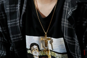 Close-up of a gold-colored steel cross pendant with twist chain worn by a male model