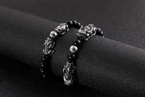 Detailed view of black beaded bracelet with silver Pixiu charm on a dark display