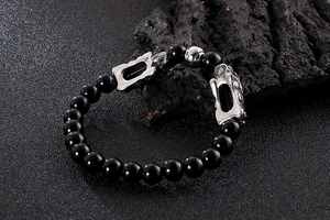 Macro shot of black beaded bracelet with silver Pi Xiu charm on charcoal stones