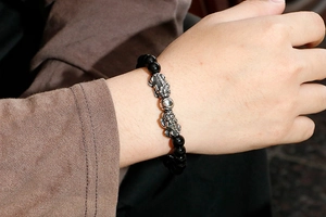 Close-up of beaded bracelet with silver PiXiu charms on wrist showing glossy black beads