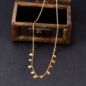 Macro shot of minimalist gold necklace with multiple round discs on a vintage wooden box