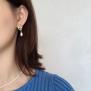 Macro view of gold wrinkled stud earrings with baroque pearl drops on a model